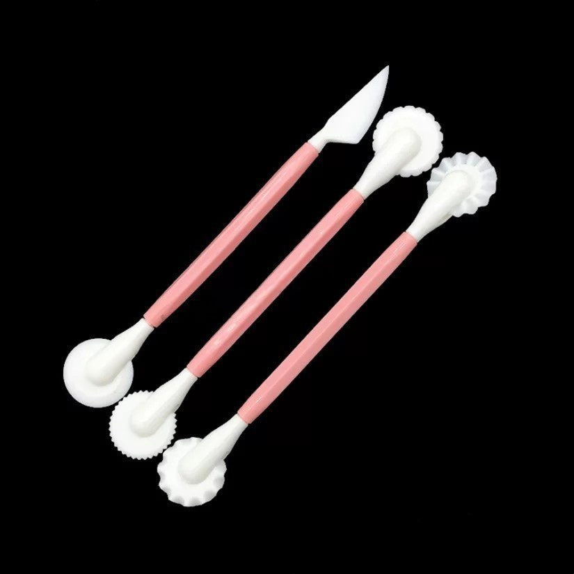 Three pink and white ceramic sculpting tools with textured white heads, arranged diagonally on a solid black background.